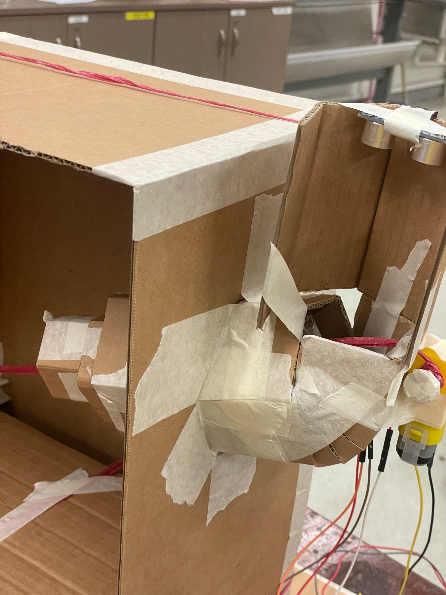The cardboard feeder arm, taped to the side of the cage, with an ultrasonic sensor at the top