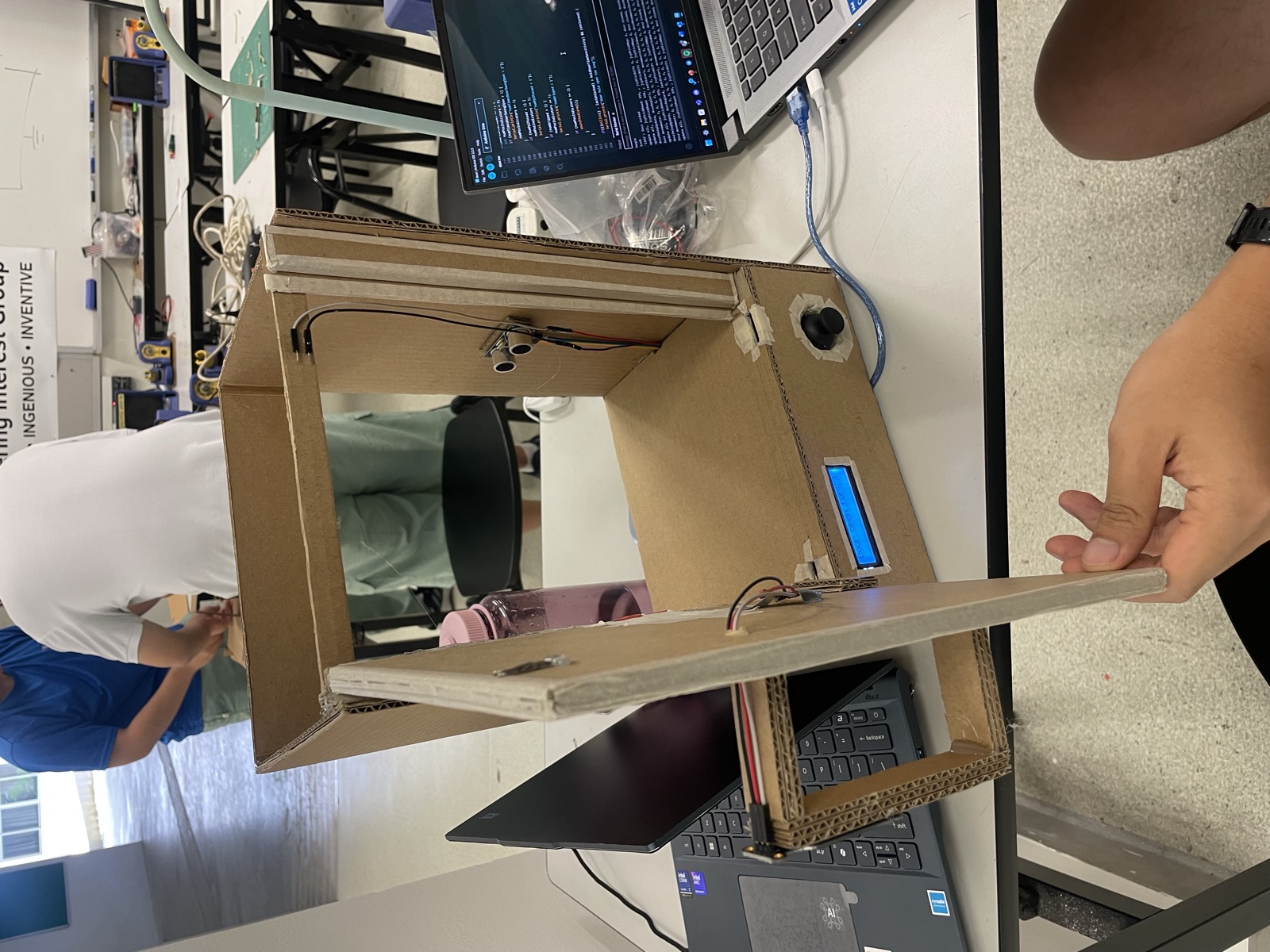 The gate frame on a desk mid-build, with a teammate holding the door panel